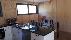 Une cuisine moderne avec un plan de travail noir, des appareils en acier inoxydable, une table à manger en verre et un lambris en bois.