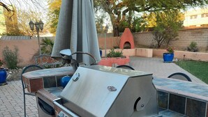 An outdoor grill with a tiled backsplash and a chimney, surrounded by potted plants and a brick wall.