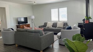 Ein modernes Wohnzimmer mit grauen Sofas, einem Flachbildfernseher, einer Stehlampe und einem schwarzen Kaminofen.