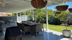 Eine Terrasse im Freien mit überdachtem Sitzbereich, einem Tisch und hängenden Pflanzgefäßen mit Blumen.