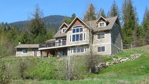 Una casa grande de dos pisos con un balcón, rodeada por un paisaje boscoso.