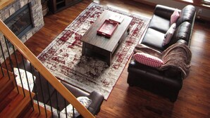 Una sala de estar amplia con chimenea de piedra, un ventanal grande, un televisor de pantalla plana, un sofá de cuero y una mesa de centro de madera.