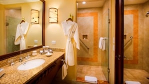 A hotel bathroom with a sink, mirror, robe, and shower area. - Ocean View Suites to Accommodate Any Party Size On the Beach (Cabo San Lucas)