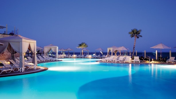 A large, clear swimming pool with lounge chairs and umbrellas around it, set against a twilight sky. - Ocean View Suites to Accommodate Any Party Size On the Beach (Cabo San Lucas)
