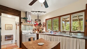 A kitchen with a wooden table, a stove, and a window overlooking greenery. - Alamo River House in Boone, NC: A charming 3BR chalet for 8 by the river! (Boone)