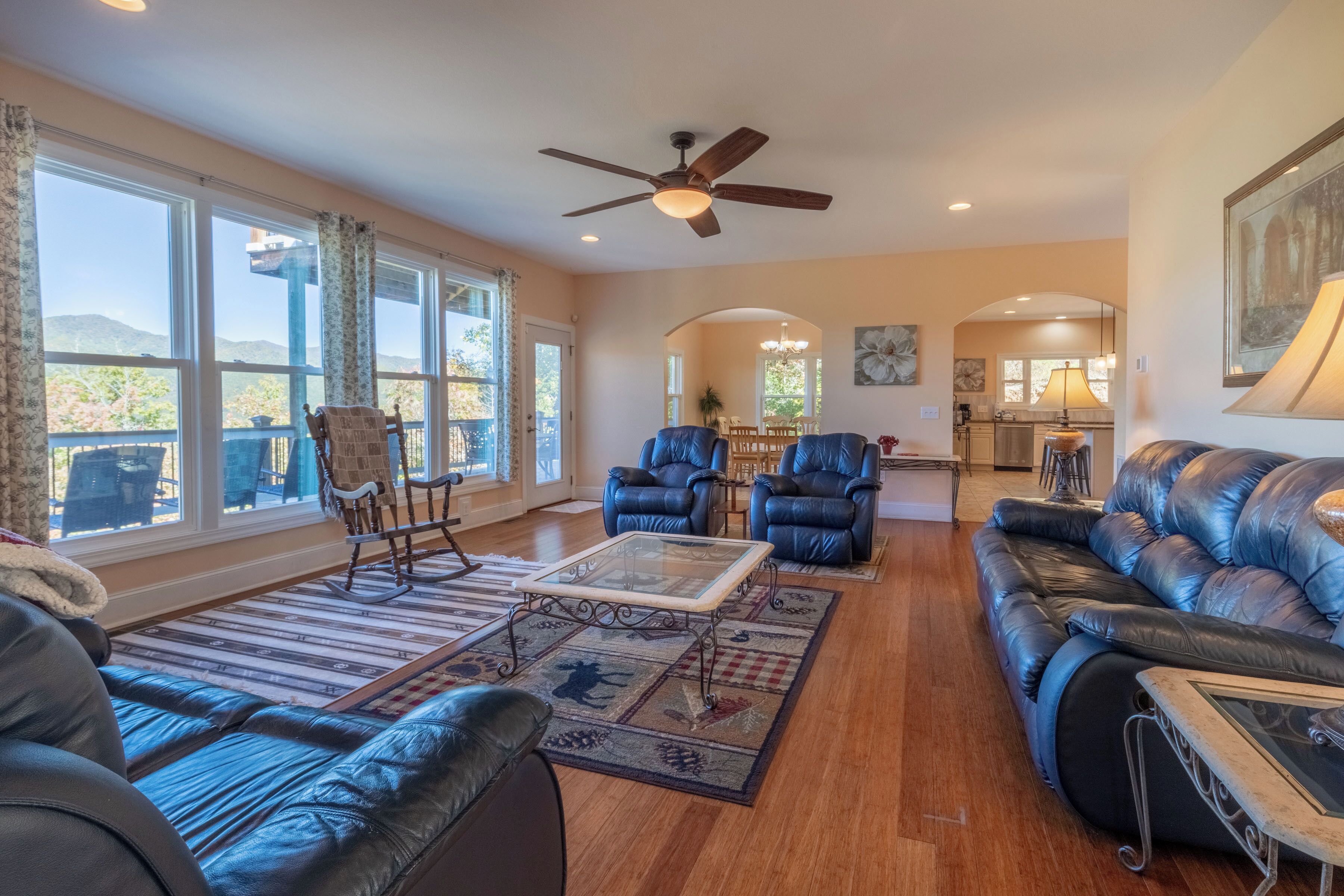 A spacious living room with leather sofas, a glass coffee table, and a ceiling fan.