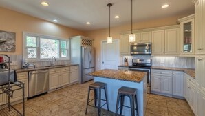 Una cocina moderna con armarios blancos, encimeras de granito, electrodomésticos de acero inoxidable y una isla central con taburetes.