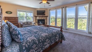 Un dormitorio con una cama grande, chimenea, ventilador de techo y vistas al exterior.