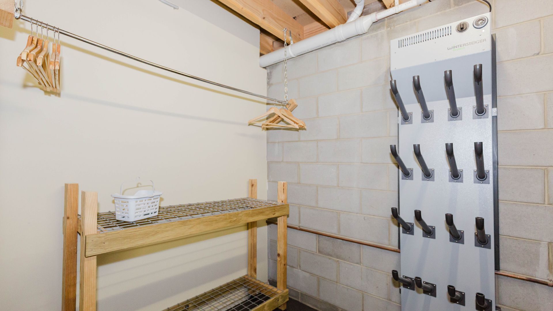 A laundry area with a wooden drying rack, a white basket, and a wall-mounted drying rack with multiple hooks.