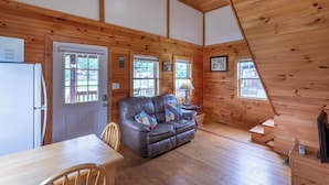 A cozy cabin interior with a leather sofa, wooden dining table, and a ceiling fan.