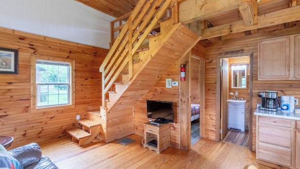 A wooden cabin interior with a staircase, a TV, a kitchen, and a dining area.