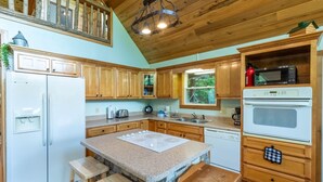 A kitchen with wooden cabinets, a granite countertop, a built-in oven, and a stone island with stools. - Mountain Time-FW- Mountain Views - Hot Tub - Fire Pit (Bryson City)
