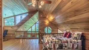 A cozy attic bedroom with a wooden sloped ceiling, a large bed with a quilt, a desk, and a chair. - Mountain Time-FW- Mountain Views - Hot Tub - Fire Pit (Bryson City)