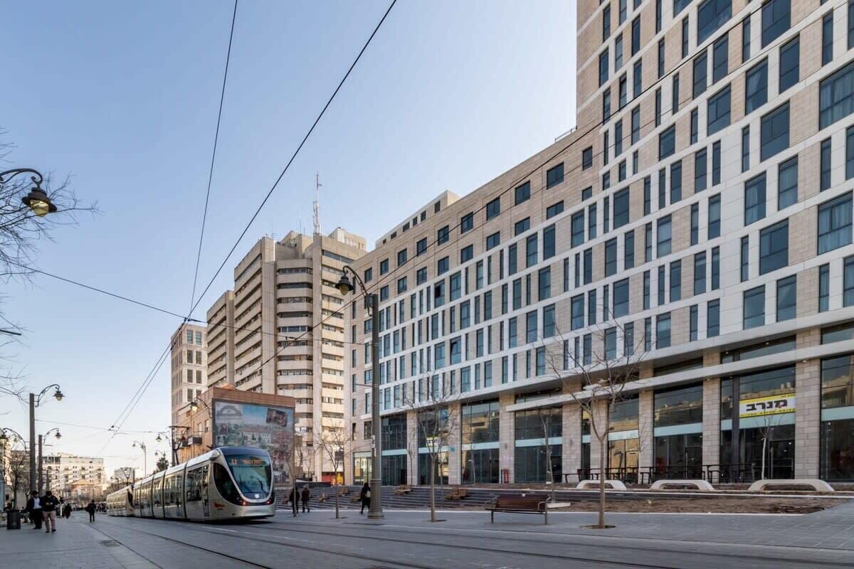 A modern urban street with a tram, high-rise buildings, and a clear sky.
