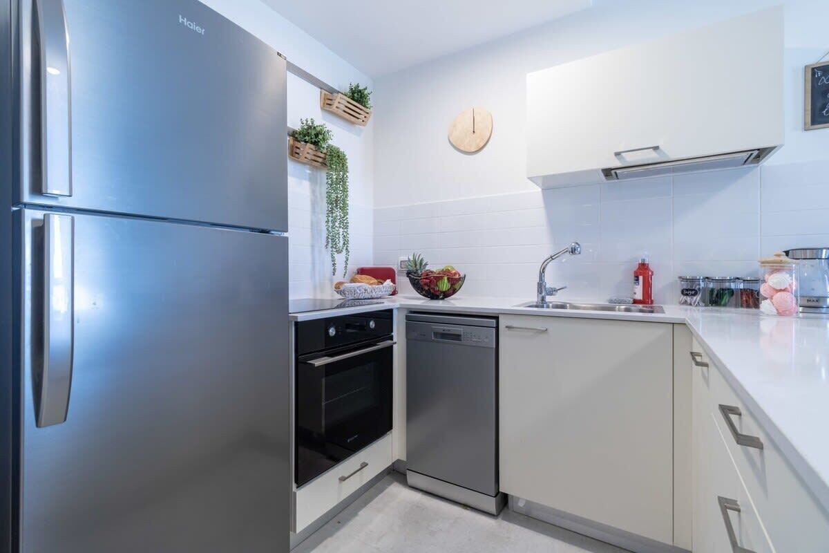 Eine moderne Küche mit einem Edelstahl-Kühlschrank, einer Spülmaschine und einem eingebauten Backofen. An der Wand hängt eine Uhr und auf der Arbeitsfläche steht eine kleine Pflanze.