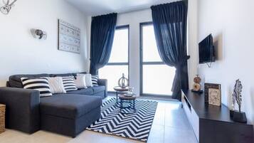 A modern living room with a grey sectional sofa, a black and white chevron rug, a small round coffee table, and a flat-screen TV mounted on the wall.