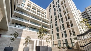 Un edificio moderno de varios pisos con balcones, ventanas amplias y un patio empedrado con jardineras.