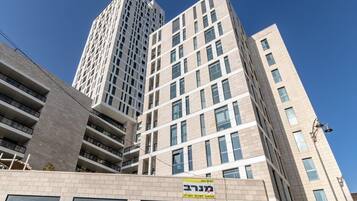 A multi-story building with a modern architectural design, featuring a mix of window patterns and a prominent yellow sign with Hebrew text.