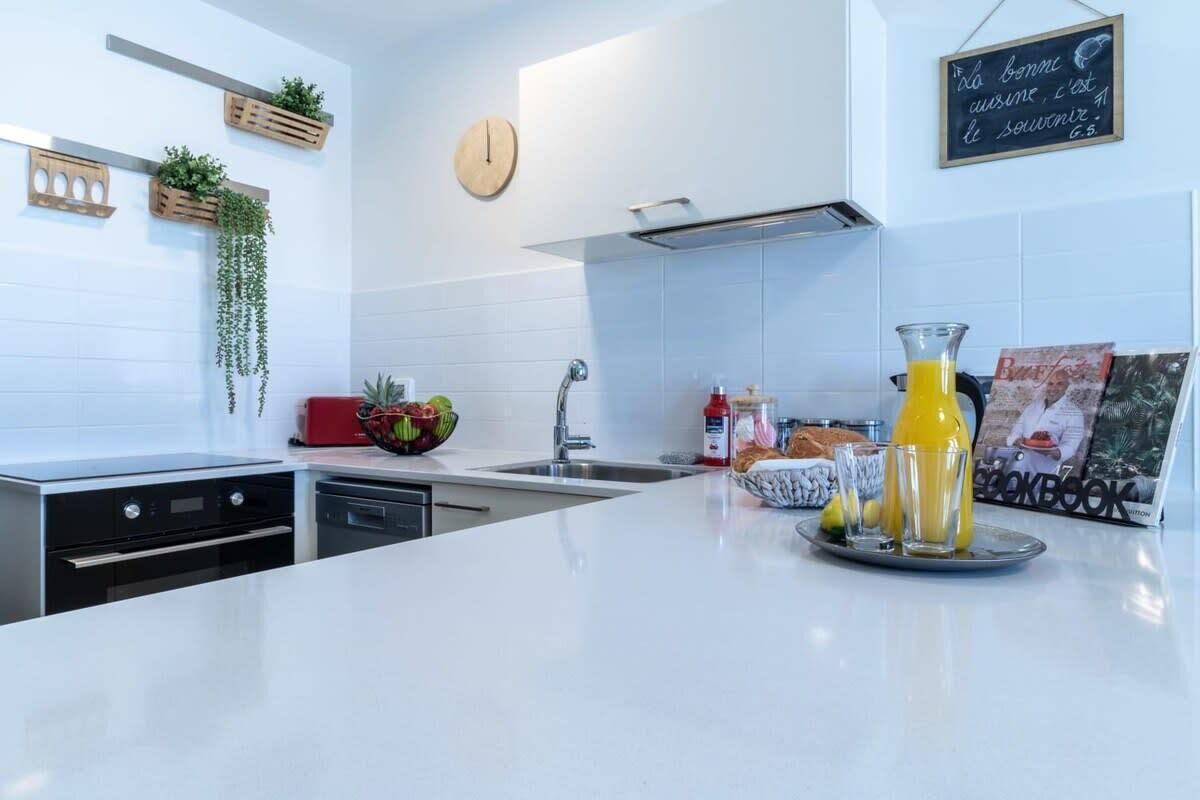 A modern kitchen with white countertops, a built-in oven, a sink, and hanging plants.