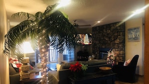 Ein gemütliches Wohnzimmer mit Kamin aus Stein, einer großen Topfpflanze und einem Weihnachtsbaum.