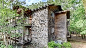 Eine rustikale Holzhütte mit Steinsicht und Holzfassade, umgeben von Bäumen.