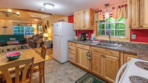 A kitchen with wooden cabinets, a refrigerator, a sink, and a dining area with a table and chairs. - Cabin on the Creek-Creek side- Hot tub - Fire Pit - Sleeps 4 (Whittier)