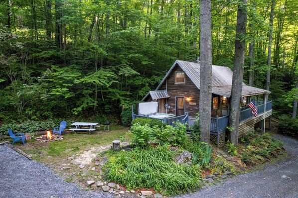 A cabin with a deck, surrounded by dense forest.