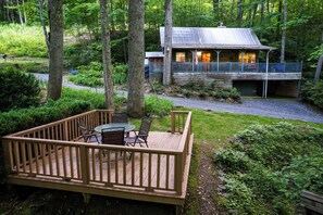 A wooden deck with a table and chairs, surrounded by lush greenery and trees.