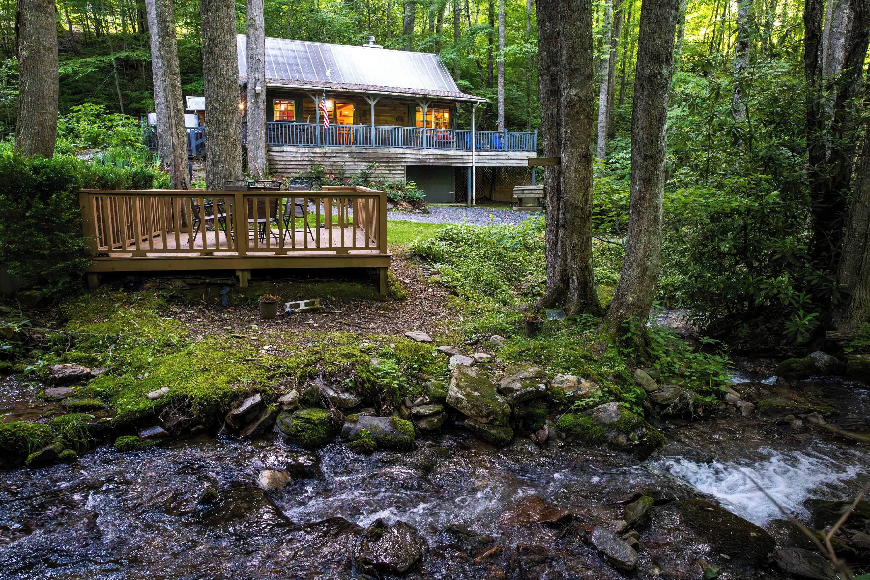 A cabin with a deck overlooking a forested area and a stream.