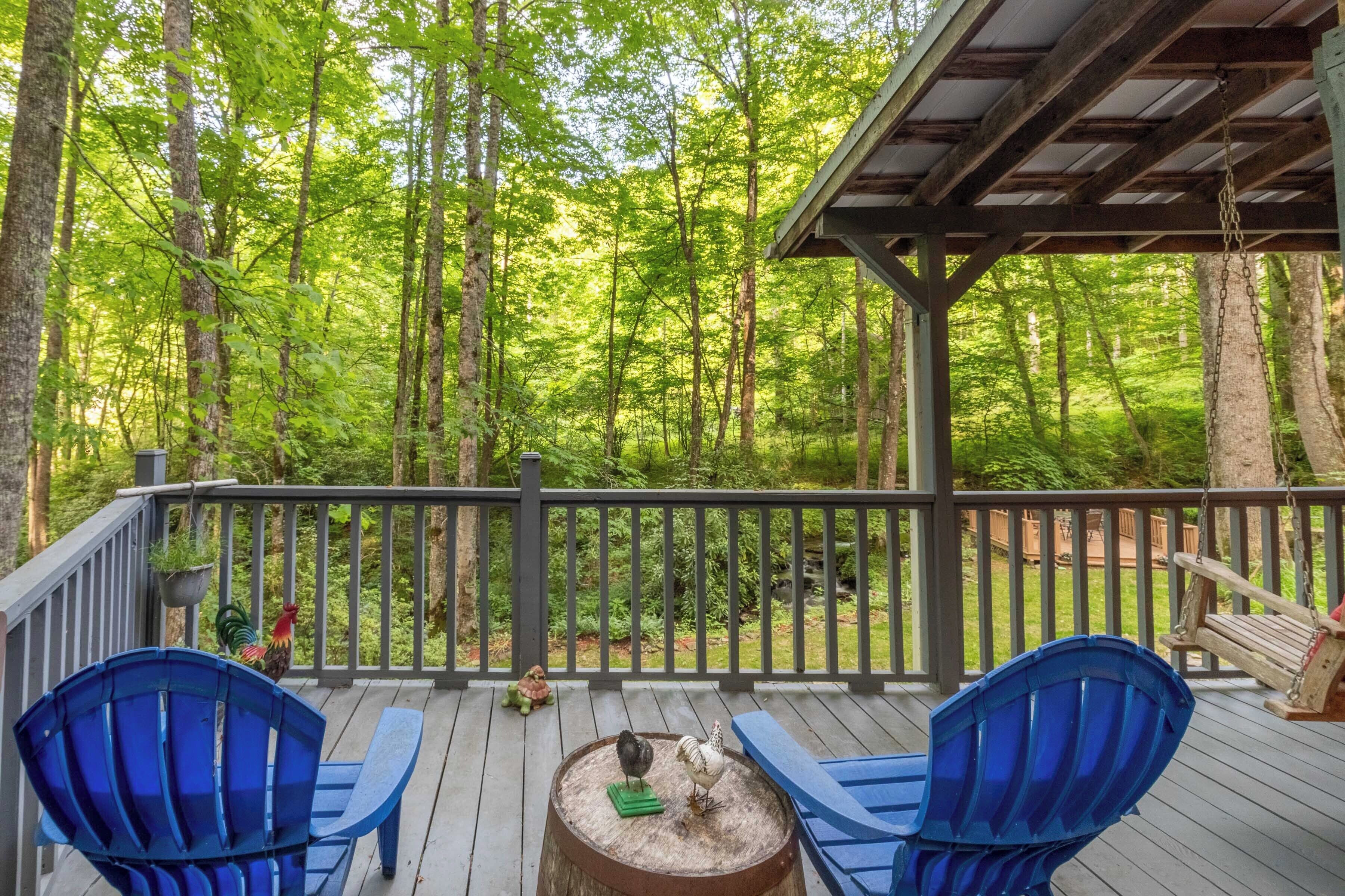 Eine Holzterrasse mit zwei blauen Adirondack-Stühlen, einer rustikalen Feuerstelle und einer Hängeschaukel.