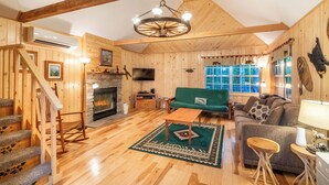 A wooden interior with a staircase, a fireplace, a green sofa, and a wooden dining table. - Cabin on the Creek-Creek side- Hot tub - Fire Pit - Sleeps 4 (Whittier)