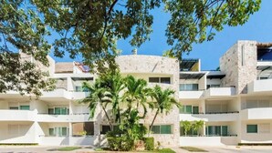 Un hotel de varios pisos con fachada de piedra, balcones y una palmera en el centro.