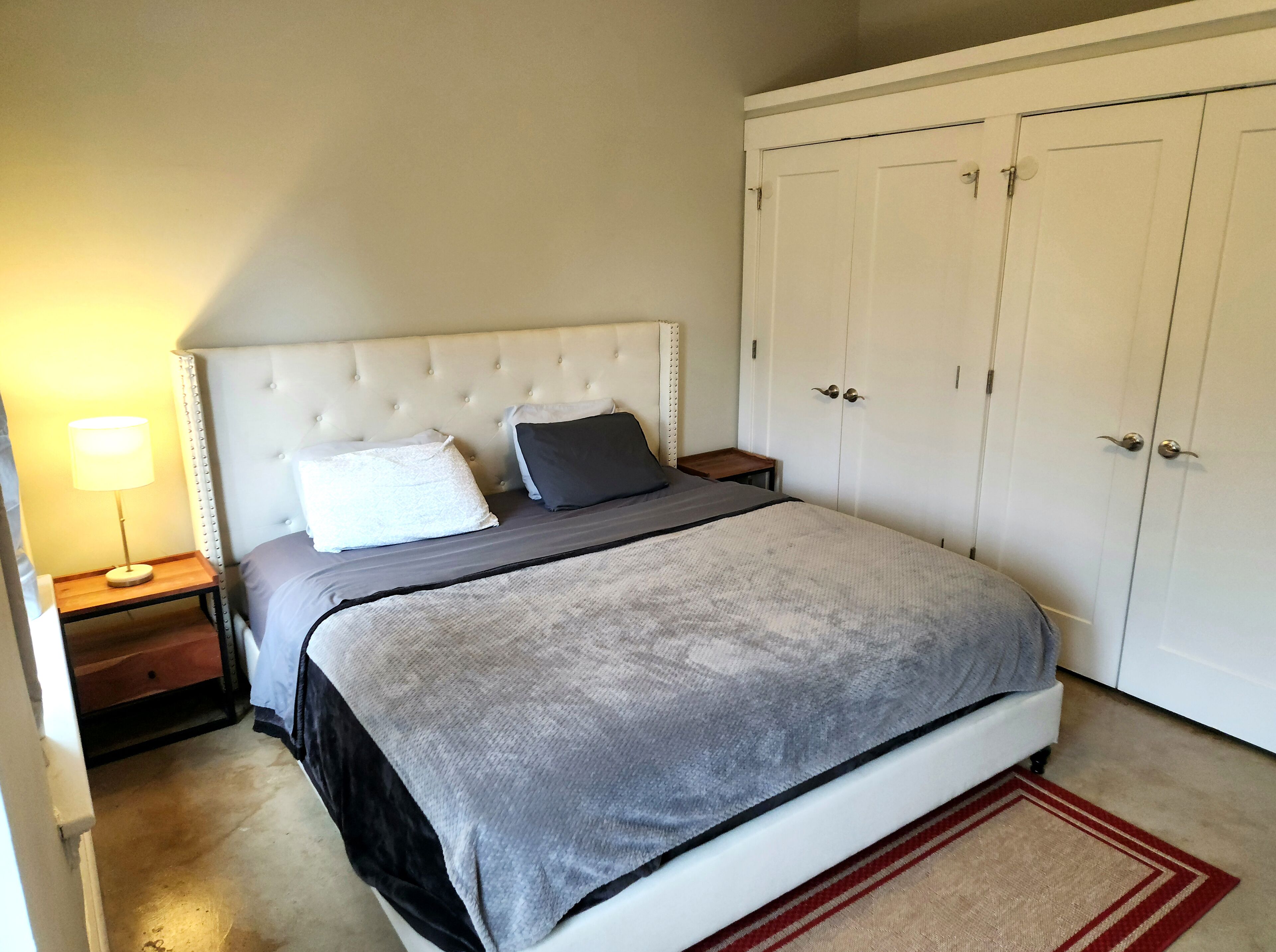 Quarto com cama, mesa de cabeceira, luminária e guarda-roupa.