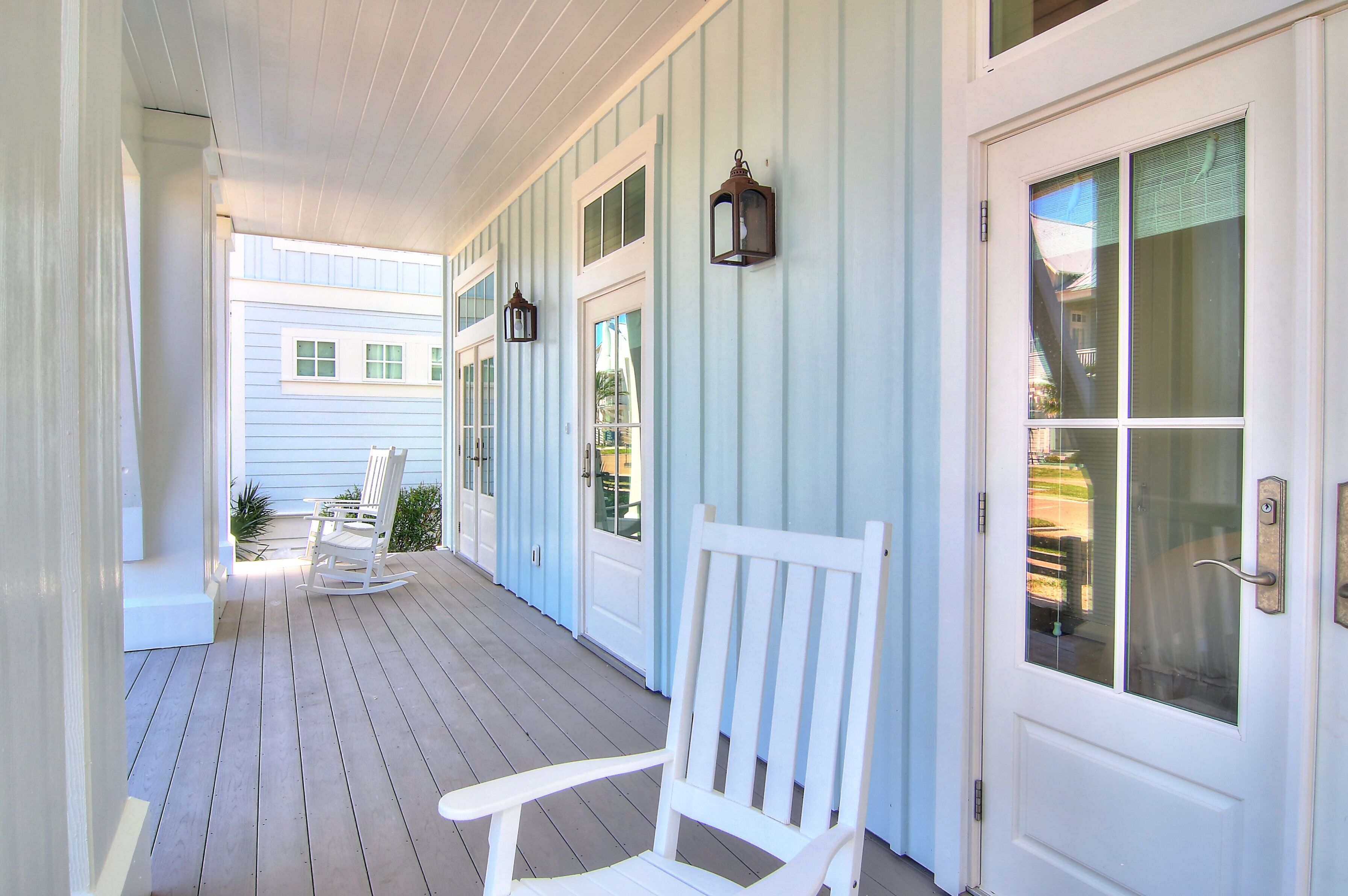 A covered porch with a white rocking chair, a door with glass panels, and a wall-mounted lantern.