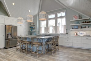 Una cocina amplia con una isla grande, armarios blancos y un refrigerador de acero inoxidable.