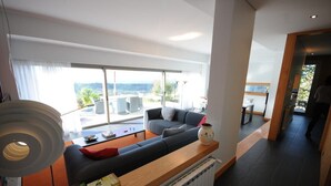 A modern living room with a sofa, coffee table, and books. There is a large window with a view of the outdoors.