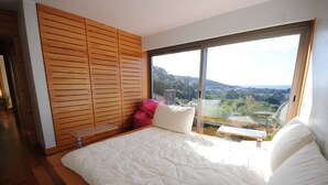 A bedroom with a large bed, wooden paneling, a bench, and a view of a landscape through a large window.