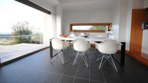 A modern kitchen with a large window, white chairs, and a dining table.