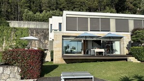 A modern house with a swimming pool, outdoor furniture, and a view of a forest.