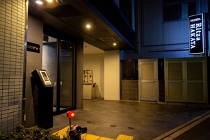 Exterior de un hotel con lector de llave electrónica, un cartel que dice 'Hotel Ritz Hakata' y una entrada con portones.