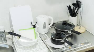 A kitchen counter with a kettle, a rice cooker, a frying pan, a cutting board, and a utensil holder.