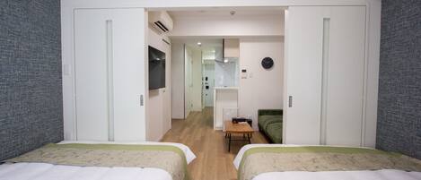 A hotel room with two beds, a small table, a green sofa, and a clock on the wall.