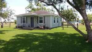 Une petite maison de plain-pied, dotée d’un porche à l’avant, entourée d’une pelouse bien entretenue et d’arbres.