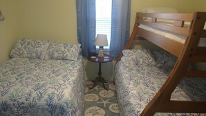 Une chambre avec deux lits, une petite table avec une lampe et une fenêtre avec des rideaux.