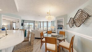 A modern kitchen with a large island, dining area with chairs, and a view to the outside. - 3133 Villamare - Direct Oceanfront Views! (Hilton Head)