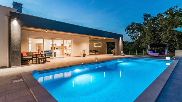 A modern house with a swimming pool, a patio with outdoor furniture, and a large glass door leading to an interior space.