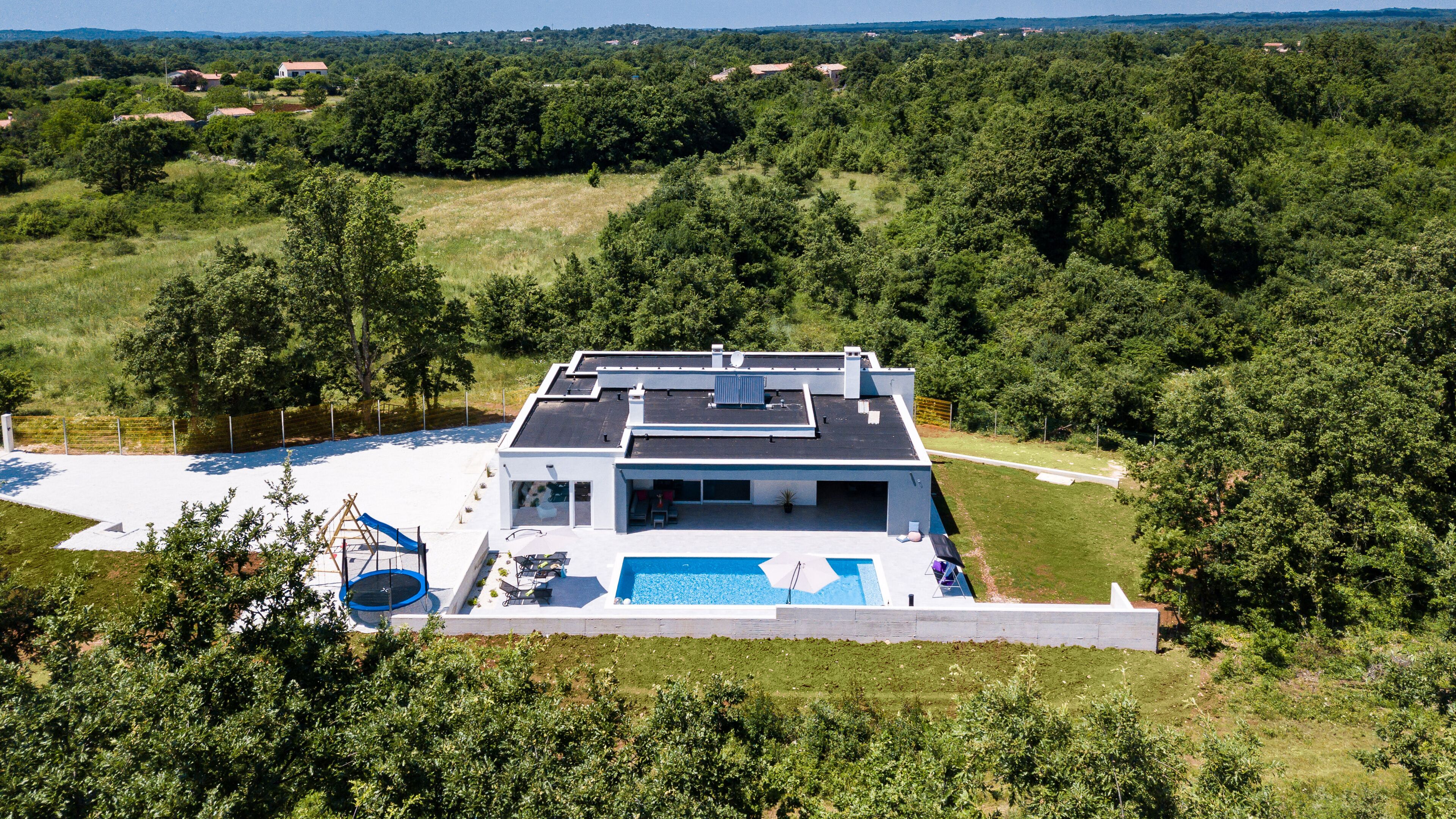 Una casa moderna con piscina, rodeada de exuberante vegetación y colinas al fondo.