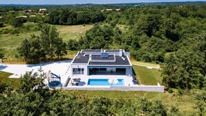 A modern house with a swimming pool, surrounded by lush greenery and hills in the background.