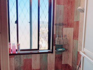 A bathroom with a window, a shower, and toiletries on the wall. - Yufuin Sunday (Yufu)