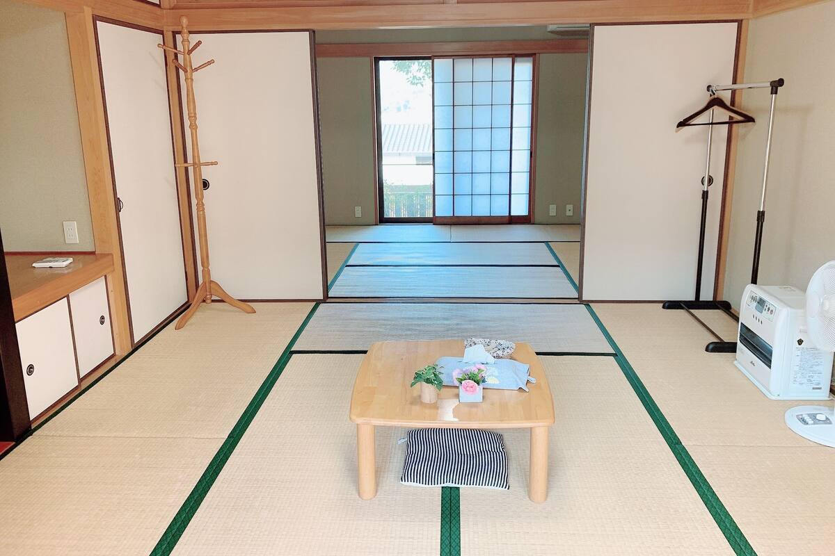 A traditional Japanese room with tatami flooring, a low wooden table with a plant, a hanging clothes rack, and a standing fan.